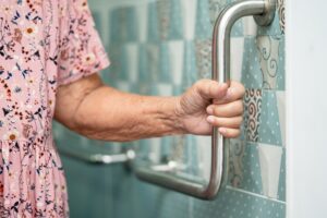 Elderly Woman Holding on to Safety Hand Rail in Bathroom