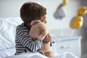 Boy sitting in hospital bed with teddy bear