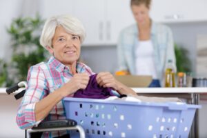 woman sits in a wheelchair, and she folds a purple garment from a blue laundry basket