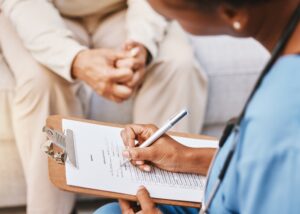 Healthcare professional filling out a checklist on a clipboard while seated with a patient