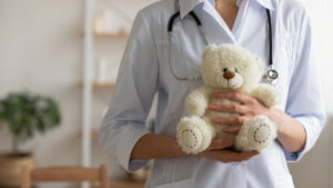 Female Medical Professional Holding White Teddy Bar in Hands.
