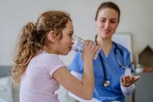 Female Caregiver Watching Little Girl Drink a Glass of Water